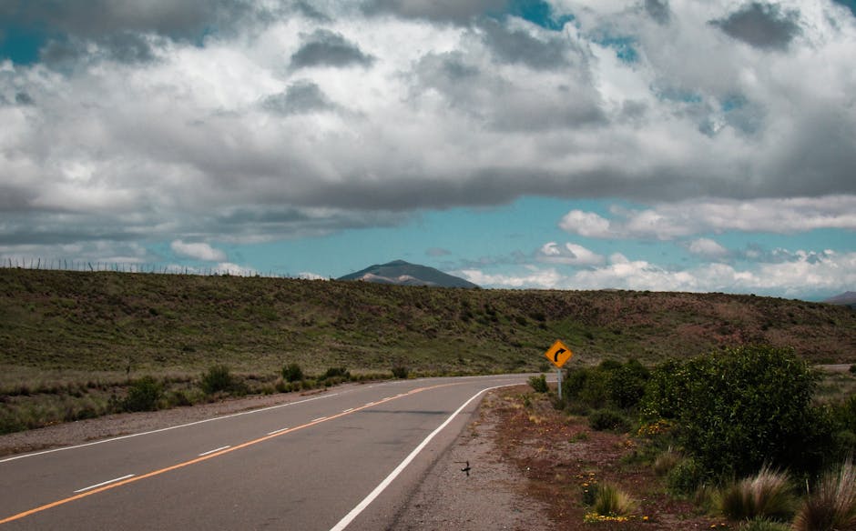A winding road through a mountainous landscape under a bright blue sky with clouds.