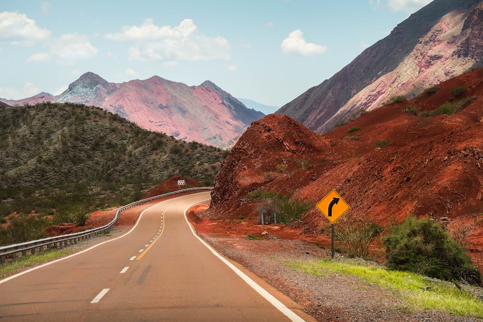 Winding road through vibrant red mountains under a bright blue sky.